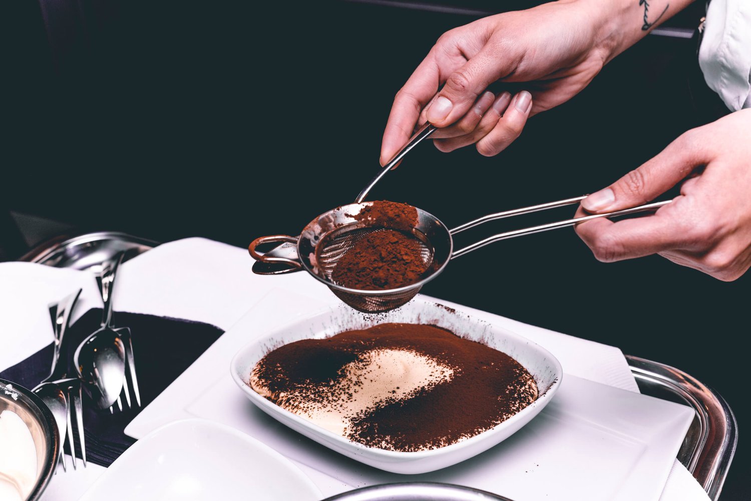 Tiramisu being finished off with a dusting of cocoa powder.